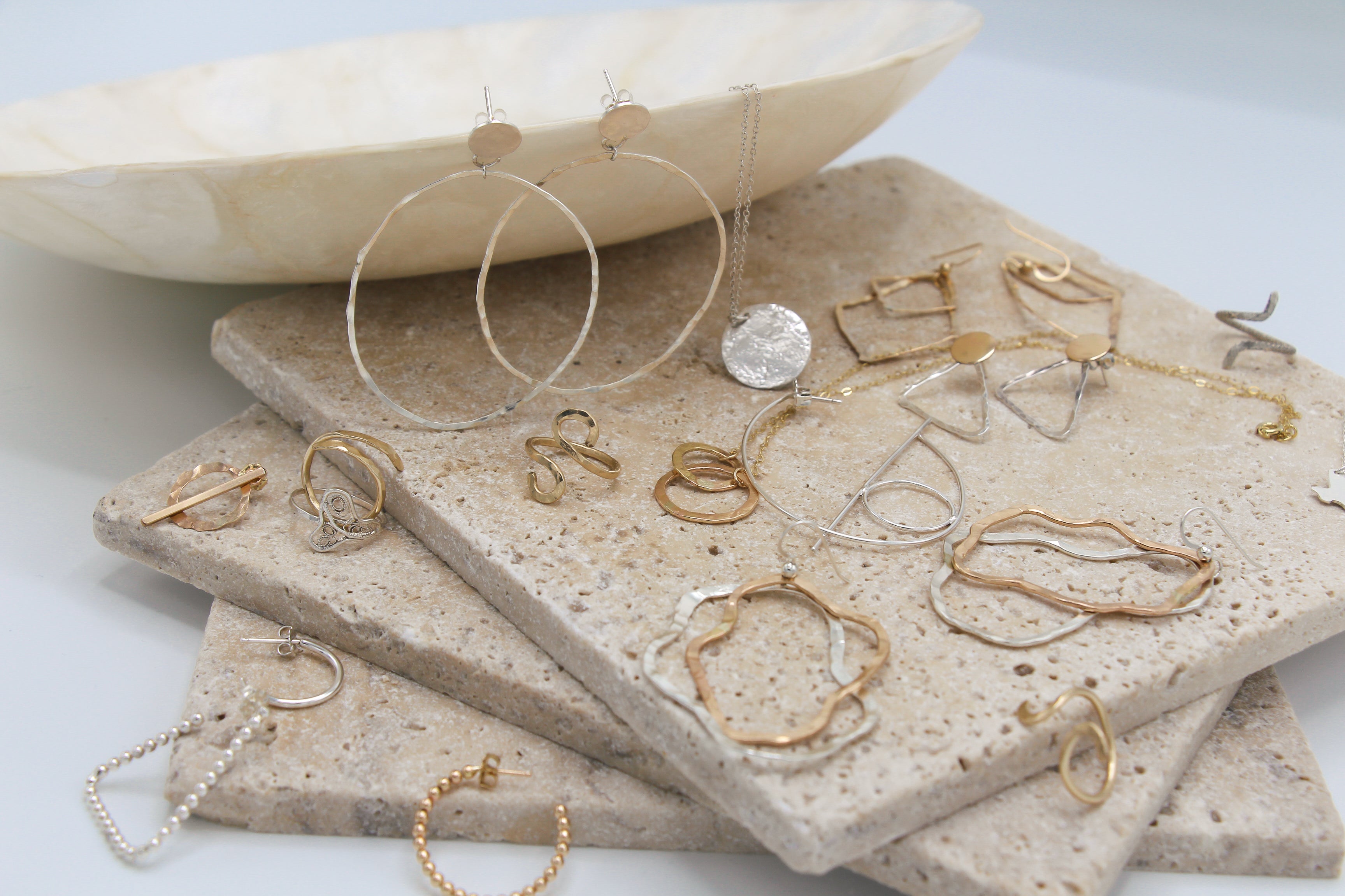Collection of gold fill and silver jewelry on stone slabs, featuring rings, earrings, necklaces  