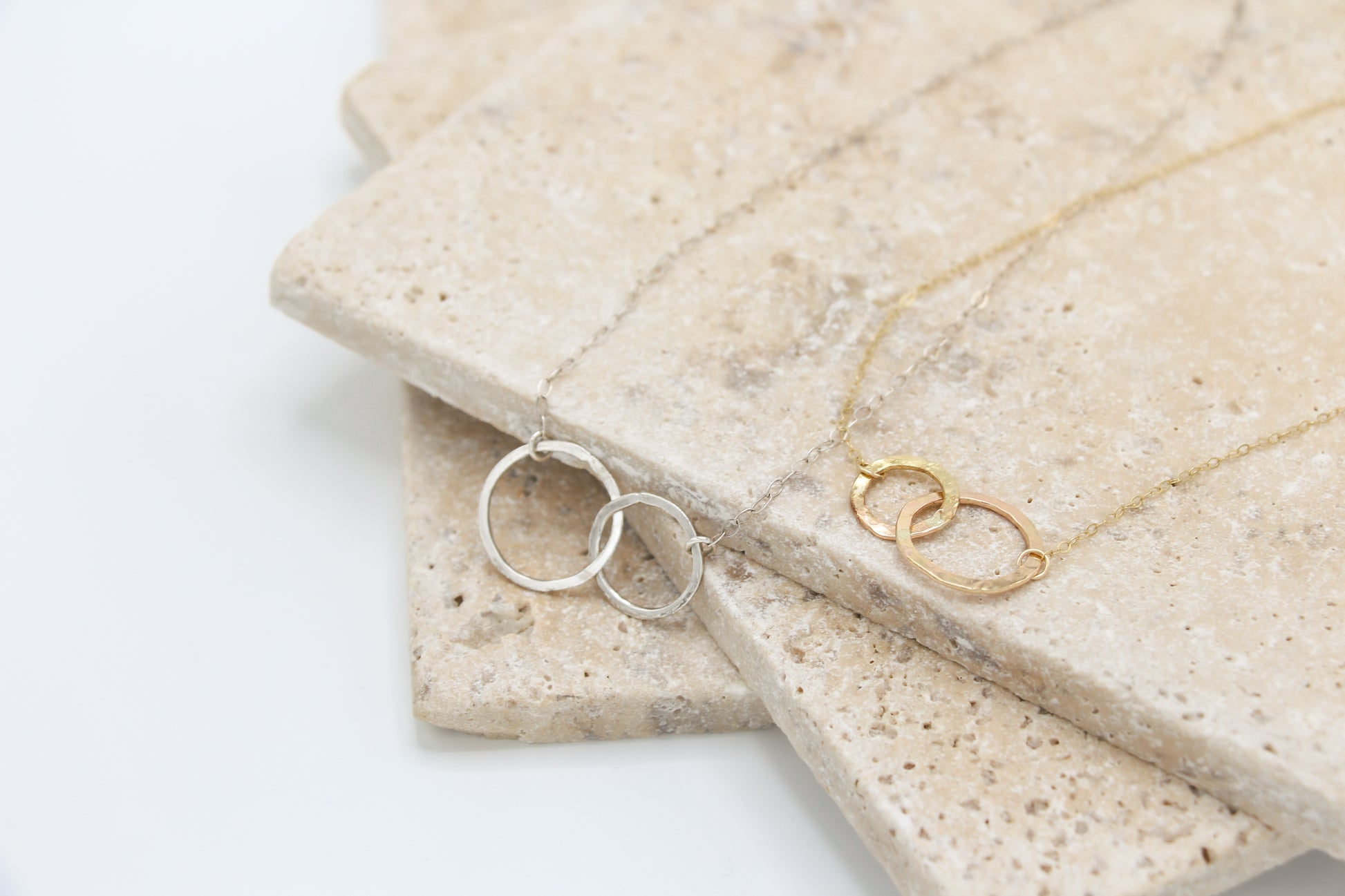 Necklace with interlocking rings on a textured stone surface, show in both gold and silver