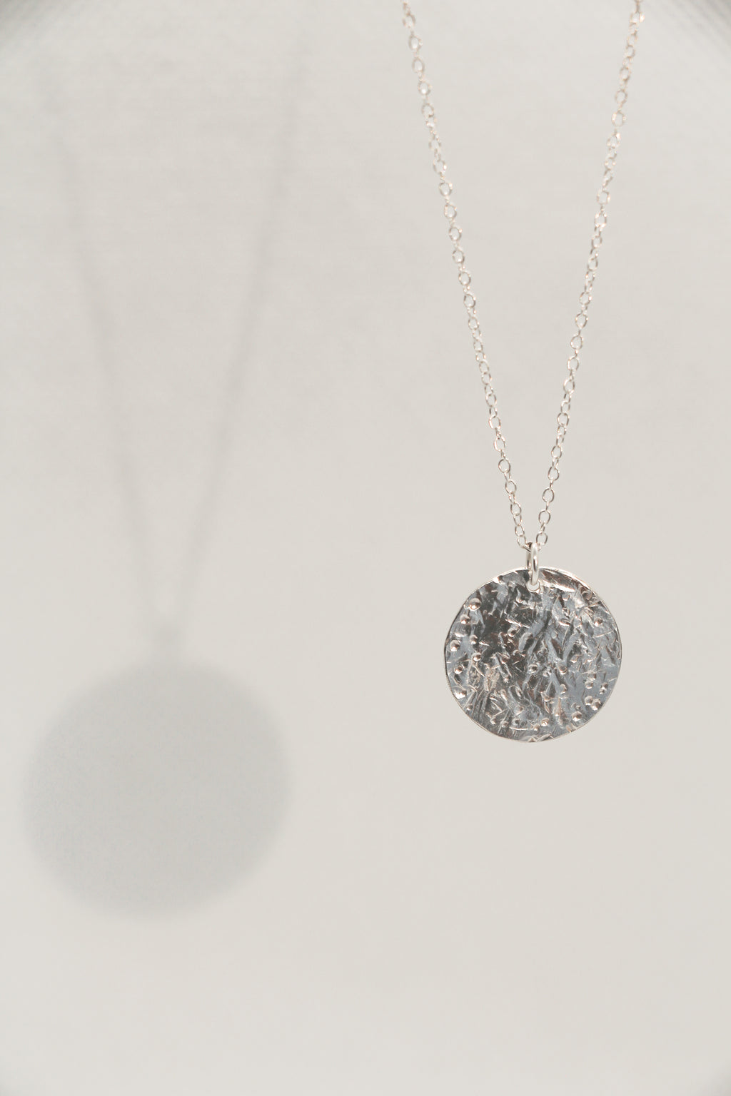 Silver necklace with a textured coin pendant on a white background