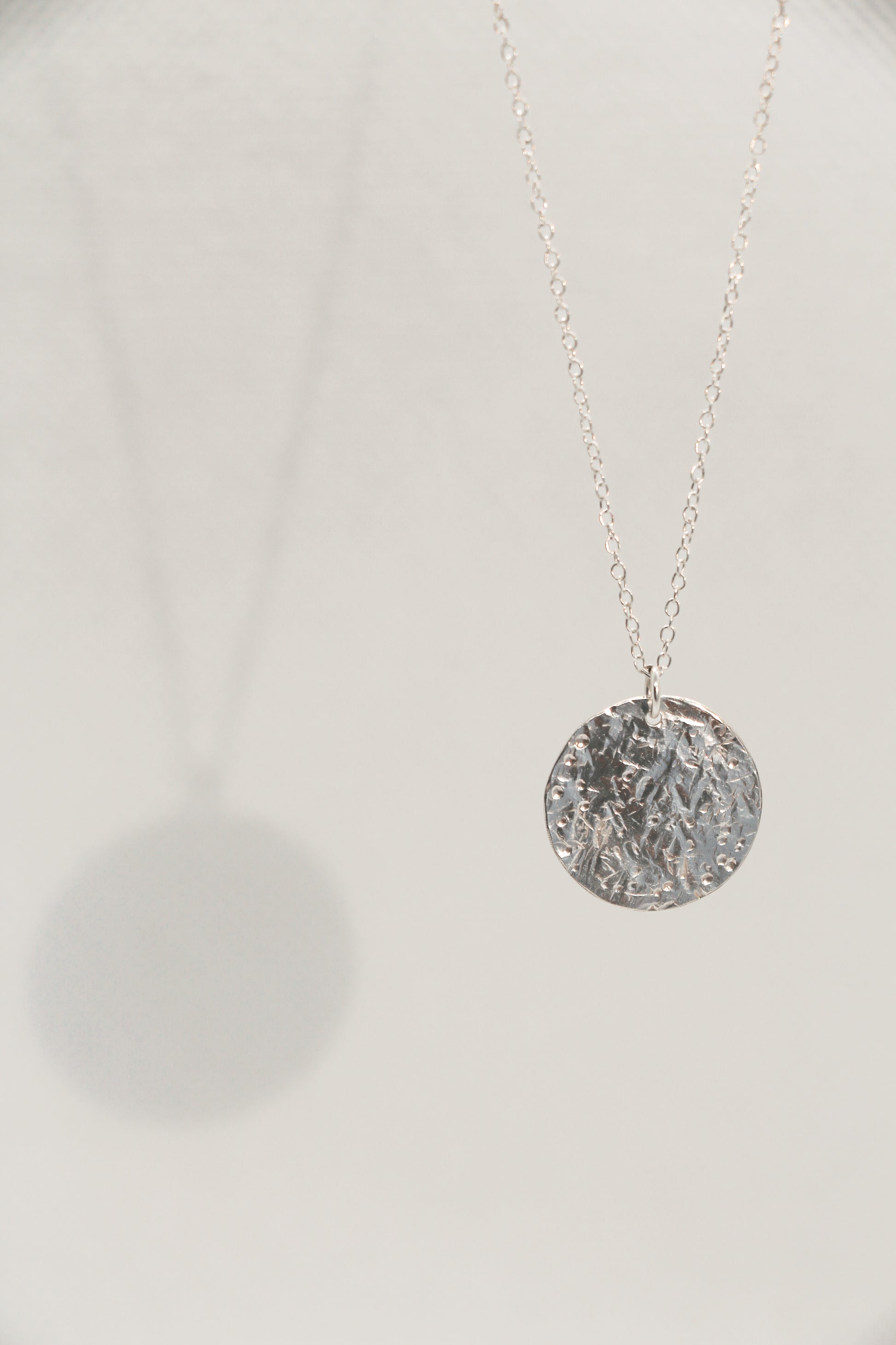 Silver necklace with a textured coin pendant on a white background