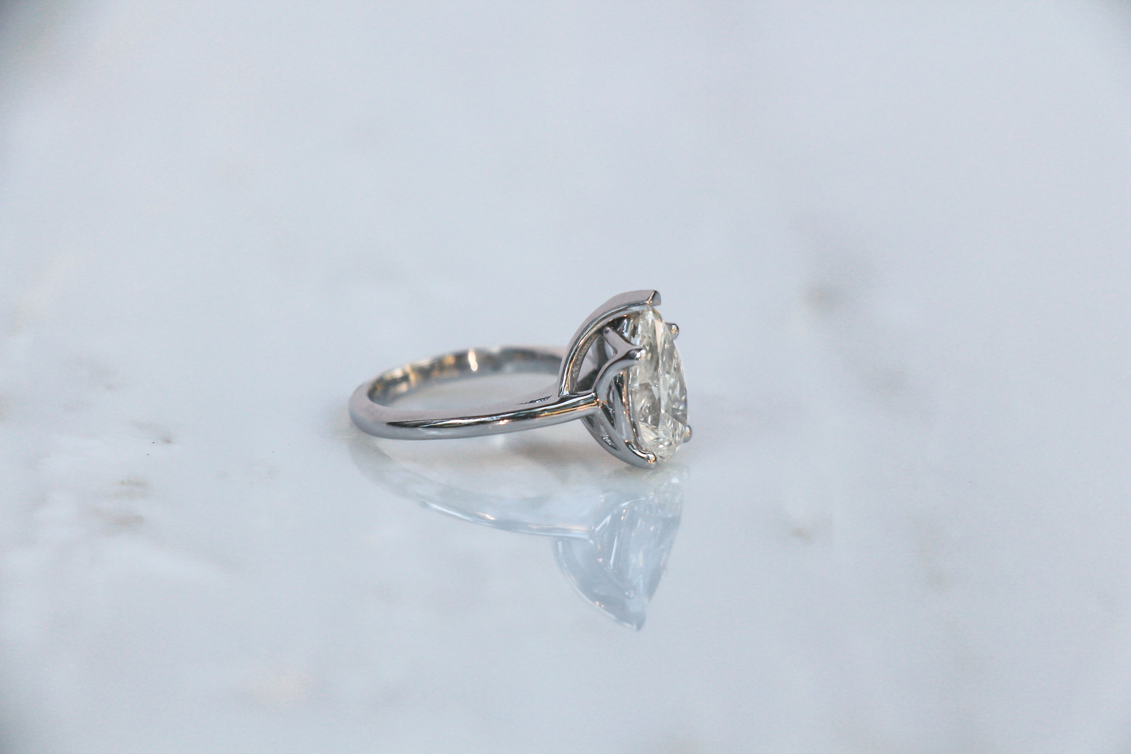 Platinum pear diamond engagement ring with a custom basket on a light marble background